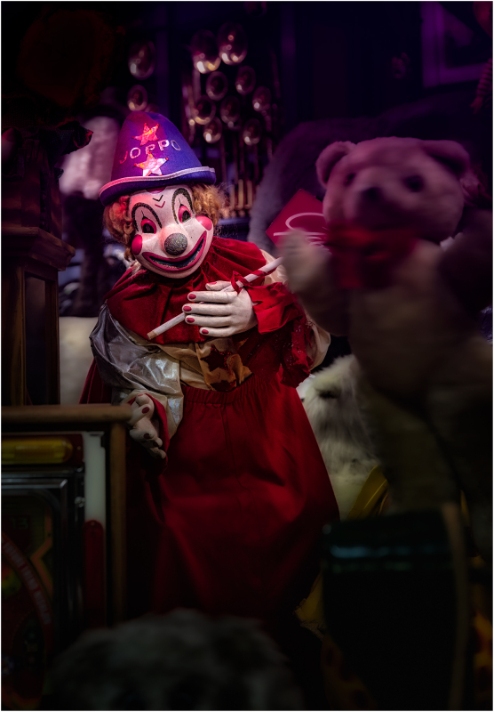 A creepy clown in a red dress, holding a toy, surrounded by shadows.