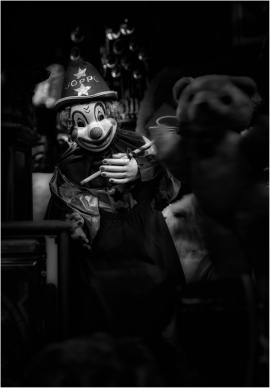 A vintage clown in a dark, moody setting, holding a toy with a haunting presence.