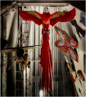 A large red parrot sculpture hangs from the ceiling in a narrow space.