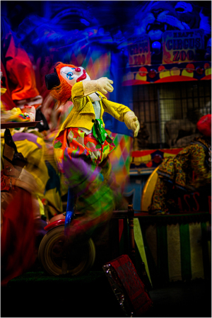 A vibrant clown puppet dances amidst a swirl of colors in a carnival setting.