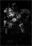 A vintage clown in a dark, moody setting, holding a toy with a haunting presence.