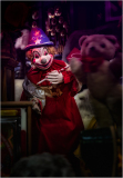 A creepy clown in a red dress, holding a toy, surrounded by shadows.