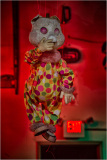 A haunting puppet dressed in a polka-dotted clown suit, suspended in eerie red light.