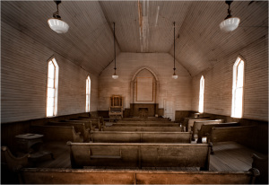 Interior of an old church with wooden pews and arched windows, showcasing historical architecture.