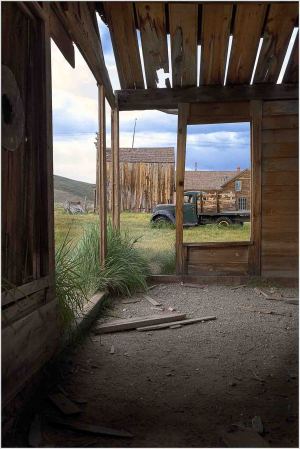View through a weathered doorway in Bodie, revealing historic buildings and a vintage vehicle outside.