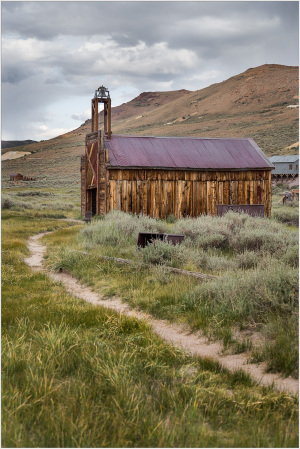 Historic wooden church in Bodie, California, surrounded by overgrown grass and mountains.