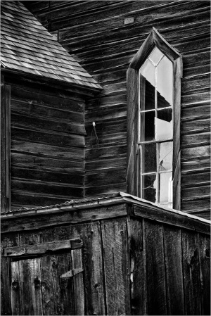 A weathered wooden structure with a pointed window reflecting its surroundings.