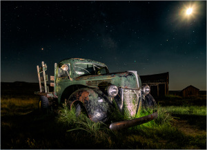 An old, rusted truck sits in a field under a starry night sky.