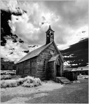 Historic wooden church in Bodie, California, surrounded by clouds and ghost town remnants.