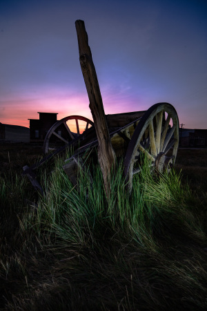 An old wagon wheel partially buried in grass at dusk, hinting at past civic life.