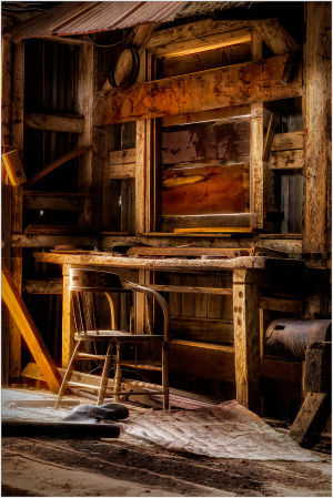 Interior of a historic wooden structure with a chair and workbench, showcasing craftsmanship.