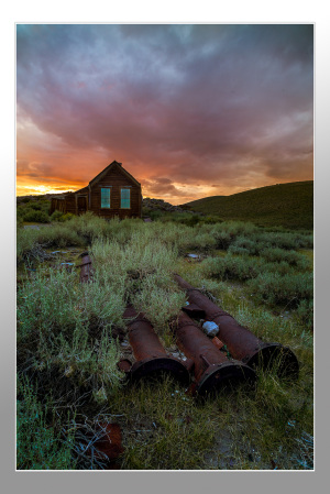 Rusty pipes in foreground with a historic building at sunset in Bodie, California.