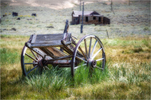 An old, rusted wagon wheel rests in a grassy field, hinting at past agricultural life.