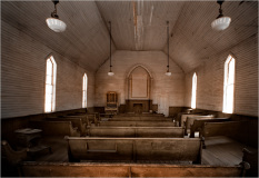 Interior of an old church with wooden pews and arched windows, showcasing historical architecture.