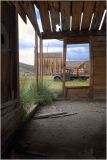 View through a weathered doorway in Bodie, revealing historic buildings and a vintage vehicle outside.