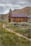 Historic wooden church in Bodie, California, surrounded by overgrown grass and mountains.