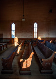 Interior of a historic church with wooden pews and sunlight streaming through windows.