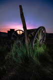 An old wagon wheel partially buried in grass at dusk, hinting at past civic life.