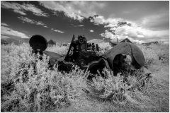 Rusting remnants of machinery in a ghost town, surrounded by dry grass and distant mountains.