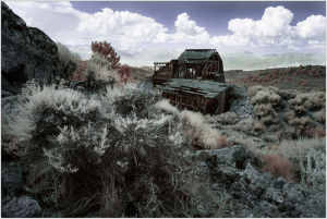 Abandoned structure amidst rugged terrain and overgrown vegetation under a dramatic sky.
