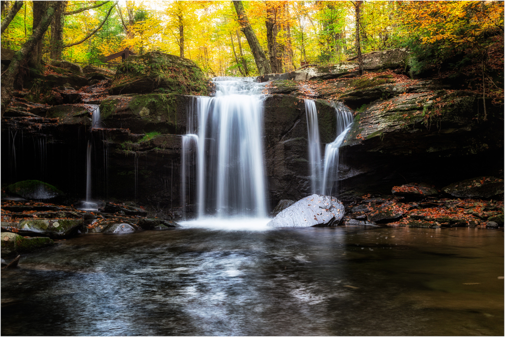 A serene waterfall cascades over rocks, surrounded by autumn foliage.