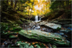 A serene waterfall cascades over mossy stones, surrounded by autumn foliage.
