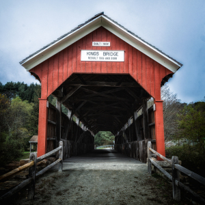 Red covered bridge stands in solitude, framed by muted skies and autumn foliage.