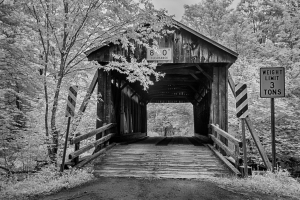 A weathered covered bridge surrounded by trees, with a weight limit sign.