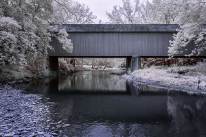 An ancient, darkened bridge looms over an eerie, reflective stream.