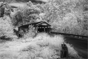 An infrared image of a covered bridge surrounded by trees and grass.