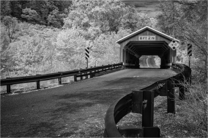A black and white image of a covered bridge with a curved road leading to it.