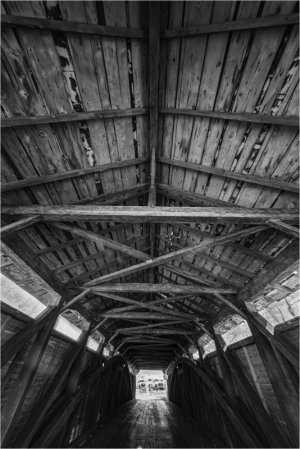 Interior view of a covered bridge with wooden beams and a light source at the end.