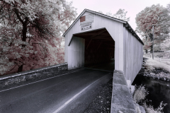 A weathered covered bridge shrouded in gentle light, surrounded by lush trees.