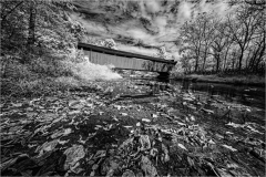 A bridge over a calm water body surrounded by trees and foliage, captured in infrared.