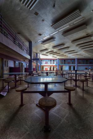 Abandoned cafeteria with empty tables and dim lighting, colorful walls in decay.