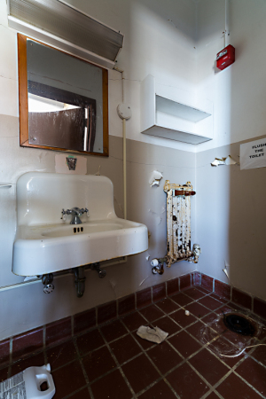An empty bathroom with a sink, mirror, and exposed plumbing on the wall.