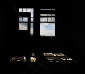 A dark room with shadowy windows and a glimmering floor reflecting light.