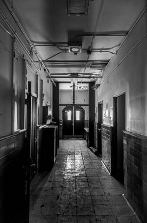 A long, dimly lit corridor with doors on either side and light filtering in from windows.