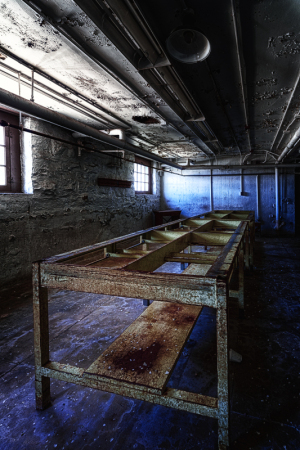 Abandoned industrial space with a long, rusted table under dim lighting