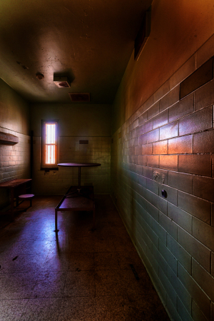 Interior view of a dimly lit prison cell with a single window.