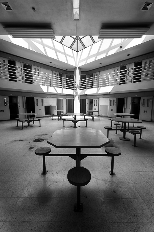 A stark, empty cafeteria with tables and chairs under a skylight.