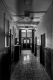 A long, dimly lit corridor with doors on either side and light filtering in from windows.