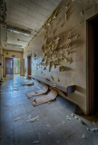 Interior corridor with peeling paint and debris on the floor, showcasing architectural decay.
