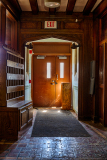 A wooden hallway with double doors and a bench, leading to an exit.
