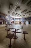 An empty room with a circular table and benches, dim lighting, and a staircase in the background.
