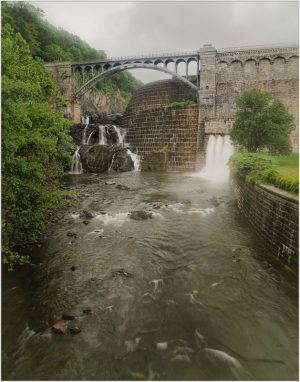 A stone bridge over a river with waterfalls cascading down.