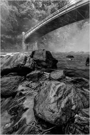 A misty river scene with a stone bridge arching over dark rocks.