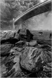 A misty river scene with a stone bridge arching over dark rocks.