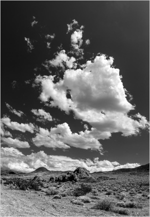 A stark desert landscape under a dramatic sky filled with clouds.