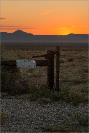 A weathered signpost stands at sunset in a vast desert landscape.